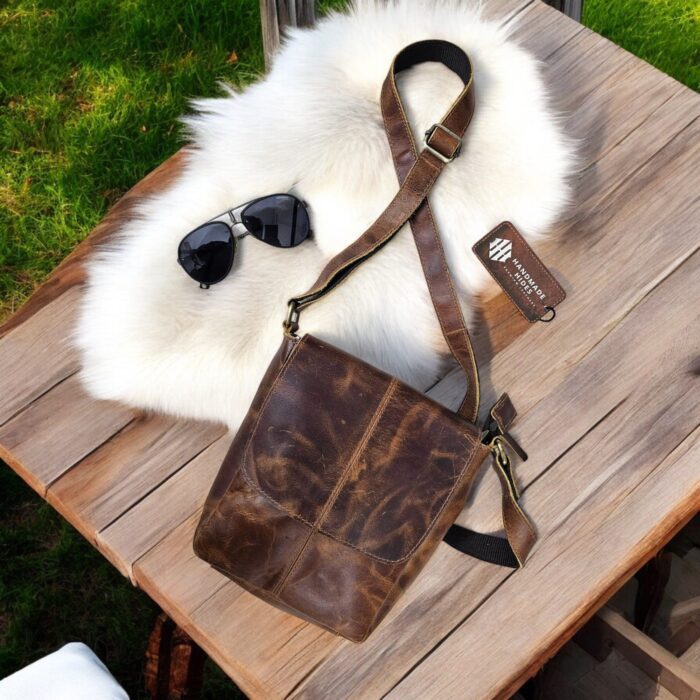 Handmade brown leather crossbody bag featuring a rustic finish, adjustable leather strap, secure flap and zipper closure, and spacious compartments.
