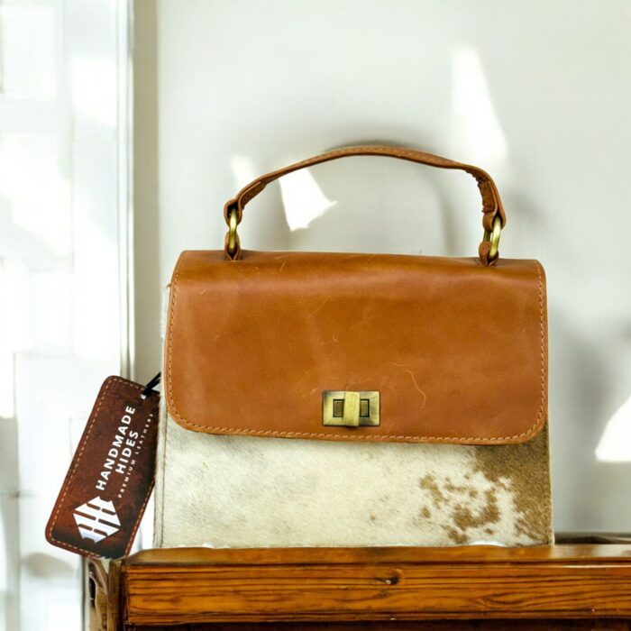 Handcrafted genuine leather handbag with rustic hair-on finish, featuring a sturdy top handle, detachable shoulder strap, and secure twist-lock closure. Elegant and versatile