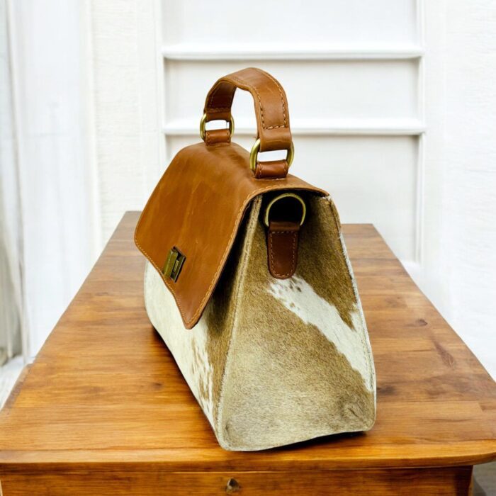 Handcrafted genuine leather handbag with rustic hair-on finish, featuring a sturdy top handle, detachable shoulder strap, and secure twist-lock closure. Elegant and versatile