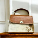 Handcrafted genuine leather handbag with rustic hair-on finish, featuring a sturdy top handle, detachable shoulder strap, and secure twist-lock closure. Elegant and versatile