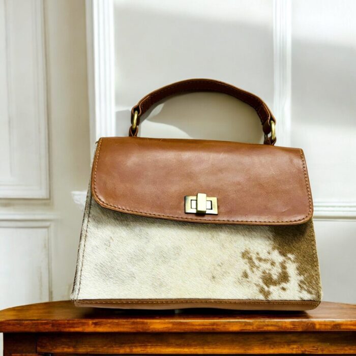 Handcrafted genuine leather handbag with rustic hair-on finish, featuring a sturdy top handle, detachable shoulder strap, and secure twist-lock closure. Elegant and versatile